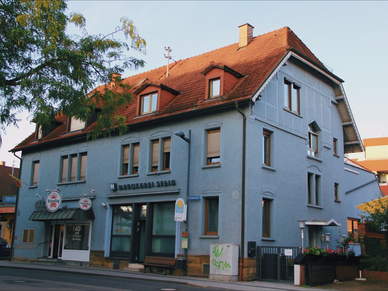 Ein längliches hellblaues Haus mit rot-braunem Dach, an der Fassade der Schriftzug "Druckerei Stein".