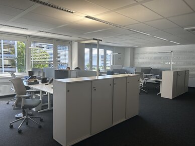 Büro mit weißen Schränken als Raumtrenner, mehreren Schreibtischen und Schreibtischstühlen. 